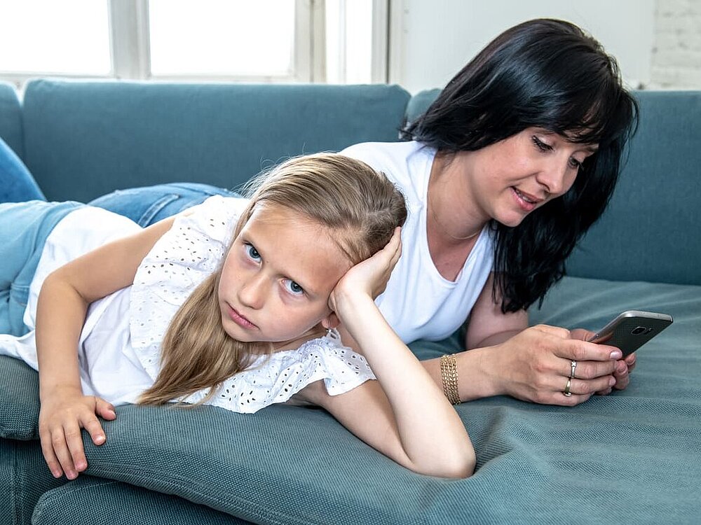 Kind ist unglücklich während die Mutter am Handy ist